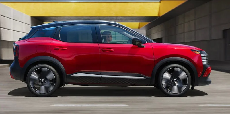 A photo of a red 2025 Nissan Kicks driving down the road.
