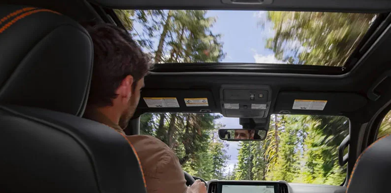 A man driving a 2025 Nissan Frontier down a road through a forest.