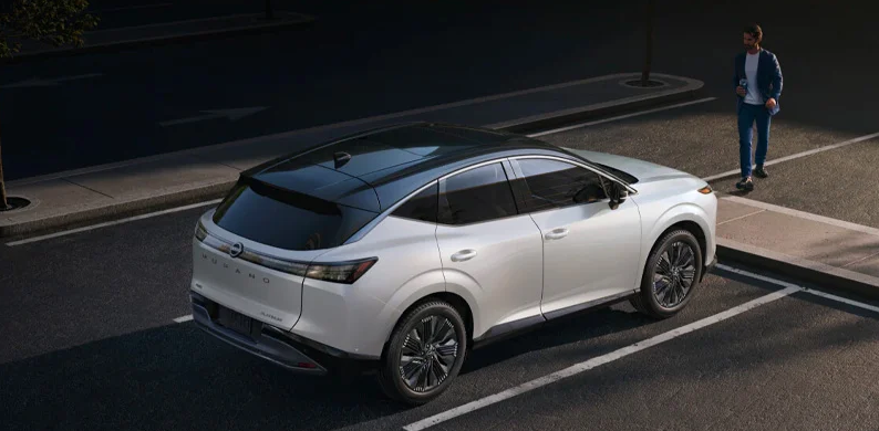 A man walking toward the front of a 2025 Nissan Murano parked in a parking lot.