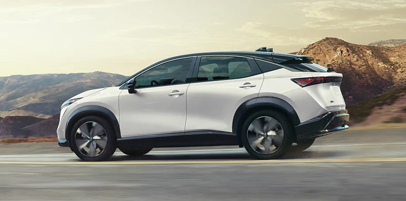 A white 2025 Nissan ARIYA driving down the road.